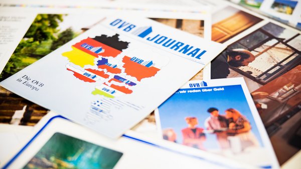 Mehrere historische Ausgaben des OVB Journals liegen übereinander auf einem Tisch.