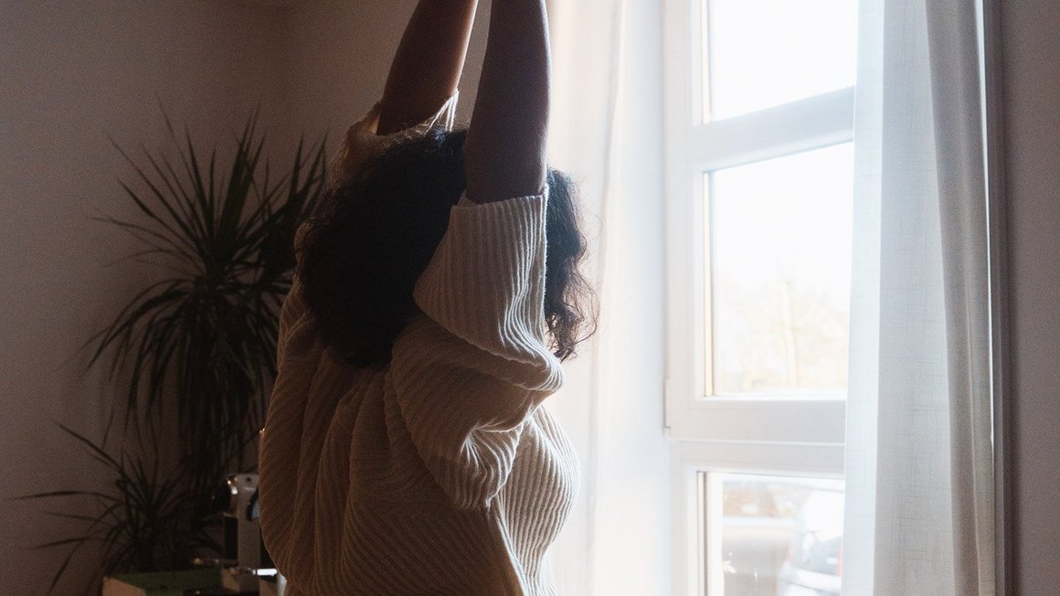 Die richtige Morgenroutine Frau streckt sich vor dem Fenster zur Morgenroutine