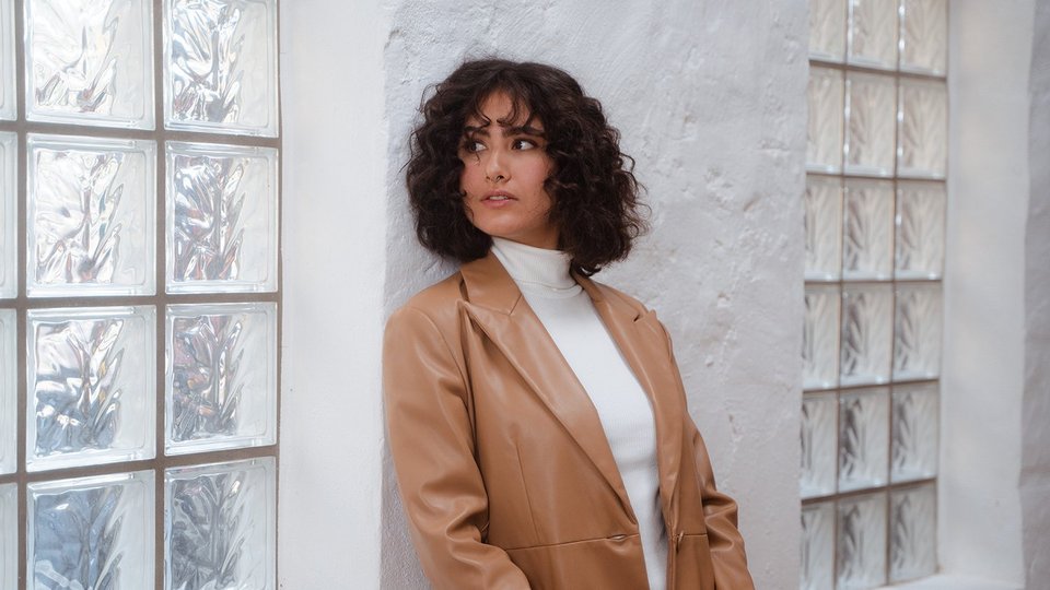 Neuorientierung vs. Jobwechsel Junge Frau lehnt an der Wand und denkt an berufliche Neuorientierung