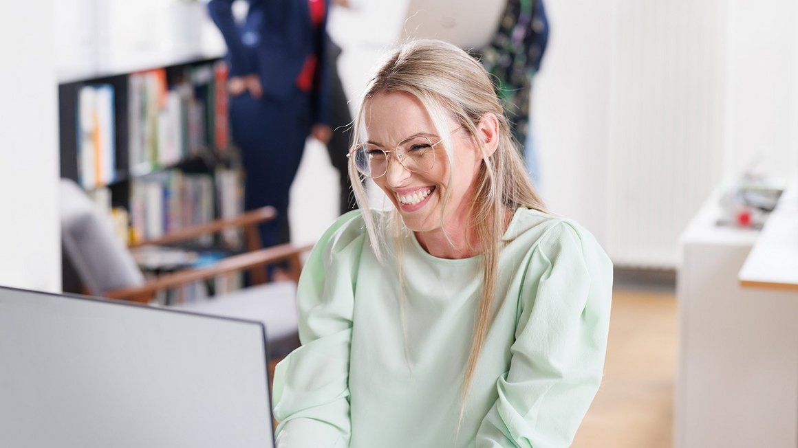 Beispiele, Herausforderungen und Lösungen für berufliche Weiterbildung Mitarbeiterin macht berufliche Weiterbildung am Laptop und lacht