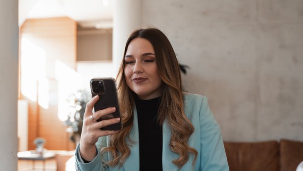 Kontakt Frau im Blazer schaut lächelnd auf ihr Handy.