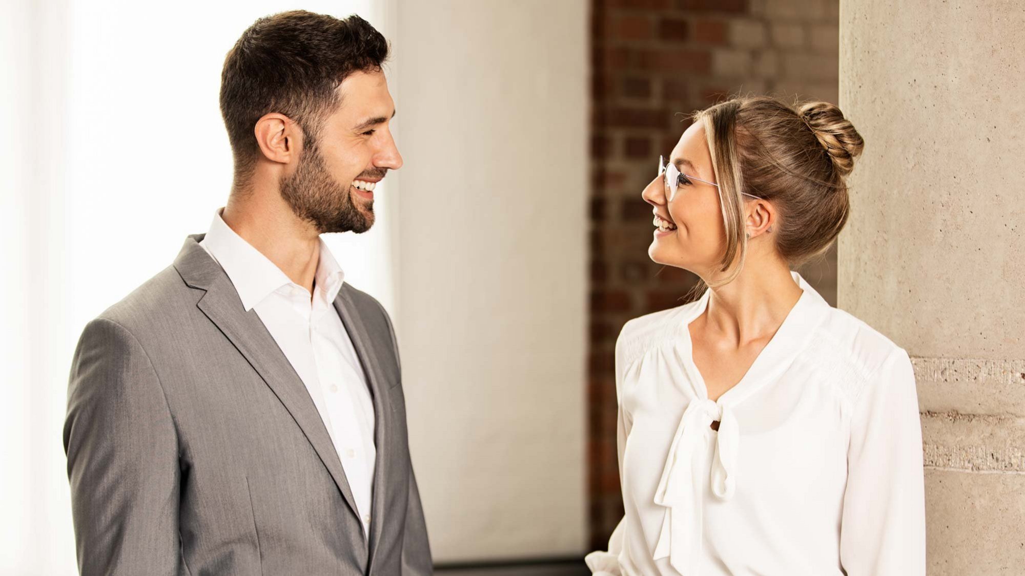 Mann im grauen Anzug und Frau in weißer Bluse unterhalten sich freundlich