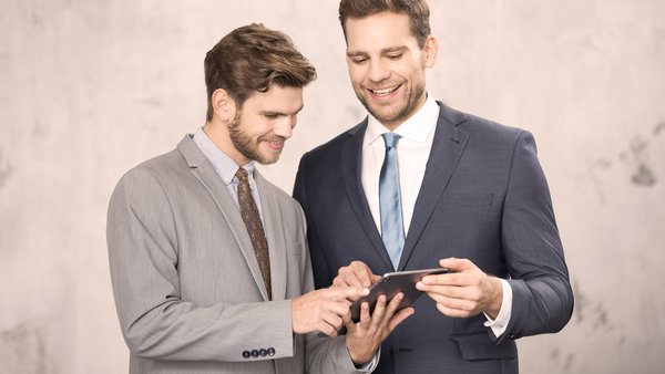 OVB Zahlen, Daten und Fakten Zwei Männer in Anzügen schauen gemeinsam auf ein Tablet und lächeln.